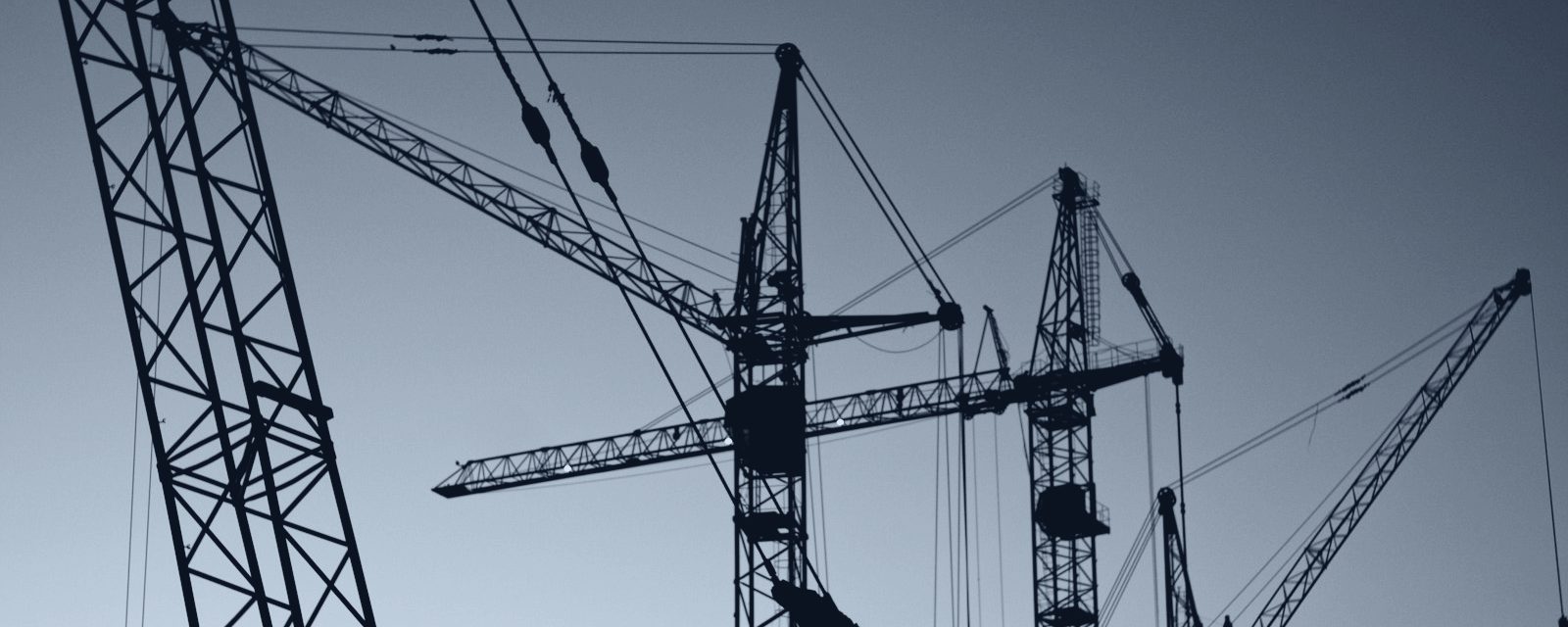 Tower cranes silhouetted in slate duotone — atmospheric imagery